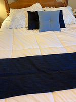Full view of queen bed with white quilted duvet, black bed runner and three decorative pillows in black and blue, set against wooden headboard.