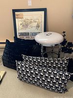 Full view of the lot showing the framed print, pillows with cat face pattern, black pillows, white cushioned metal stool, and decorative flowers