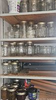 Shelf with multiple rows of glass canning jars with gold-colored metal bands and lids.