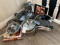 Cookware set showing various pots and pans stacked and arranged on the floor with cookbooks in the background.