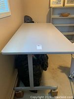 Angle view of the plain white table surface and one metal leg on caster wheels along the carpeted floor near a window.