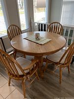 Round wooden dining table surrounded by four matching chairs with beige cushions placed in a well-lit room.