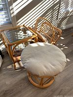 Full view of rattan side table, foot stool with beige cushion, and magazine rack with magazines inside.