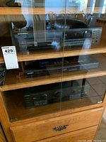 Full view of three electronic devices inside wooden cabinet with glass doors: top shelf Pioneer Multi-Disc CD Player, middle shelf Sony Blu-ray Player, bottom shelf Technics stereo receiver.