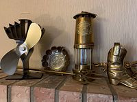 Front view of all items on a brick ledge: miner's lantern, decorative boot, brass dish, and metal fan device.