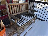 Full view of rustic wood porch bench on outdoor deck with snow on seat slats