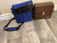 Two binocular cases side by side - West Marine blue case and brown Bushnell case.