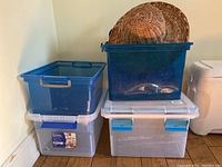 Four plastic storage bins stacked and a woven wicker hat on top