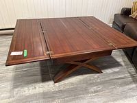 Photo of the entire wooden drop leaf coffee table with one leaf extended, showing wooden planks and metal hinges.