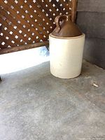 Full view of the vintage stoneware crock jug showing beige body and brown glazed top and handle.