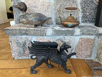 Photo showing the wooden duck decoy, copper kettle on stone hearth, and cast iron griffin figure on wood floor.