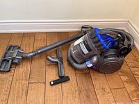 Full view of vacuum, hose, wand and three accessory tools on hardwood floor