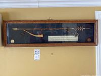 Full view of the shadow box mounted on wall containing bow, spear, arrow with feather, and medallions.