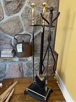 Fireplace tool set with brass finials and accents next to copper kettle on stone hearth