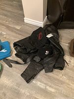 Black leather motorcycle jacket with zipper, folded on floor with Harley Davidson skull cap and black leather belt