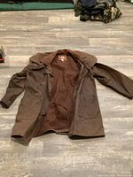 Full view of the brown 3/4 outback coat laid flat on floor showing size XL and overall condition