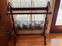 Full view of wood quilt rack showing three horizontal bars and carved ends with claw-foot legs on hardwood floor.
