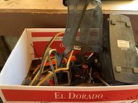 Photo showing a box containing various hand tools, clamps, jumper cables, and a black Stihl face guard on top.