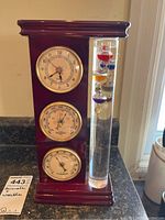 Full view of the weather station unit showing the clock, barometer, hygrometer, and Galileo thermometer within a wooden frame.