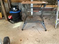Full view of Black & Decker Workmate 300 workbench in a garage setting, showing overall condition and structure including metal legs and wooden slats.