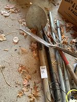 Photo of the yard tools including shovel, spade, pitchfork, and roof rake laid on garage floor with leaves around.