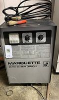 Front view of Marquette 39-110 battery charger showing control knobs, analog meter, and cables with clamps on top.