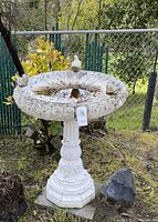 Full front view of the concrete birdbath showing the overall structure, tiered pedestal base and decorative birds on rim with water in basin.