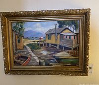 Framed oil painting showing waterfront scene with boats and houses.