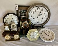 Five clocks including one large and one small marble clock, one small brass clock with visible movements, a kitchen clock and another round clock arranged together on a surface