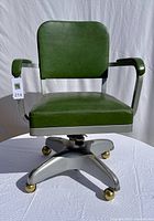 Front view of green vinyl desk chair showing padded seat, back, armrests, and metal base with caster wheels.