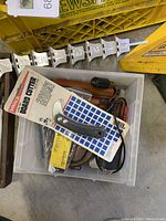 Photo of a box containing a packaged board cutter, flashlights, and other smaller tools in plastic bin
