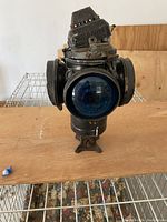 Front view of black metal vintage railroad lantern showing blue lens, ventilated perforated top, side lights, and mounting hardware.