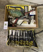 Photo shows a box with miscellaneous tools including a hand drill and a metal clamp, with a roll-up pouch of nine Stanley chisels in front.