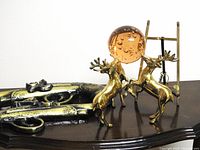 Photo showing brass deer figurines posed on hind legs with golden orb and pair of vintage brass flintlock pistols on wooden surface