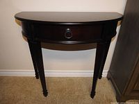 Front view of the demi-lune mahogany console table showing the drawer with metal ring pull and curved front edge.
