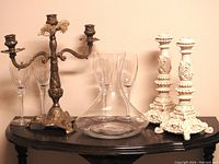 Brass candelabra, ivory candle sticks, crystal decanter, and four crystal glasses displayed on a dark wooden surface.