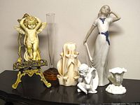 Full lot view showing infant cherub statue on brass easel, tall clear glass bud vase with amber glass bubble, hand-carved ribbon swirl candle, small thinking cherub figurine, Rex Valencia porcelain girl figurine, and Royal Worcester bone china cornucopia vase.