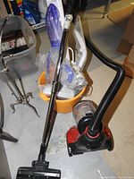 Bissell Zing II canister vacuum with taped handle and hose attachments, red bucket, and H2O floor steam mop with accessories in plastic wrapping inside the bucket.