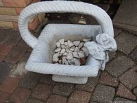 Front and top angled view of concrete basket planter with white stones inside, showing rope-like textured edges and floral decoration on corner.
