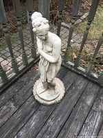 Full view of the full-size concrete garden statue 'Shy Venus' standing on a circular base outdoors.