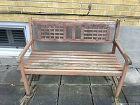 Front view of wooden garden bench showing slatted seat and lattice backrest, placed outdoors on concrete pavers.