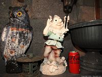 Photo showing black/orange detailed plastic owl figurine next to a plastic gnome lamp holding a lantern, with a Coca-Cola can for scale, and a green plastic plant urn.