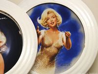 Close-up of a framed plate showing Marilyn Monroe in a sparkling gold dress against a blue background, signed by Chris Notarile.