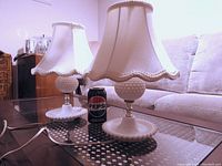 Two vintage hobnob milk glass lamps on glass table next to couch, with Pepsi can for size reference