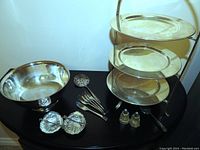 Full view of the multi-layer dessert stand, silverplated large bowl, set of four forks, pierced serving spoon, salt and pepper shakers, and four shell-shaped silver dishes on table.