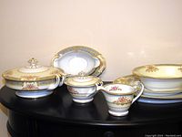 Full view of all serving pieces on black table showing white porcelain with gold trim and floral decorations