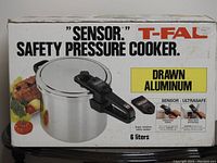 Box front showing T-Fal Sensor Safety Pressure Cooker, 6 liters, drawn aluminum, with image of pressure cooker and chicken and vegetables.
