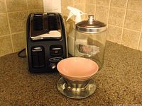 All four lot items on kitchen counter: T-Fal two-slice toaster, glass biscuit jar, Eaton's stainless steel bowl with pink insert, and white plant spritzer.