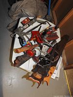 Photo showing a collection of hand tools arranged on a table including hand wood saws, hacksaw, red stapler, hand crank drills, and other assorted small tools.