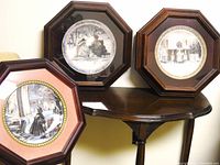 Three octagonal wooden framed collectible plates showing winter scenes by Trisha Romance on a table